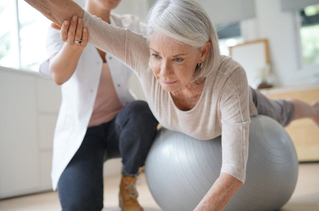 Ältere Frau trainiert mit ihrem Physiotherapeuten und einem Schweizer Ball